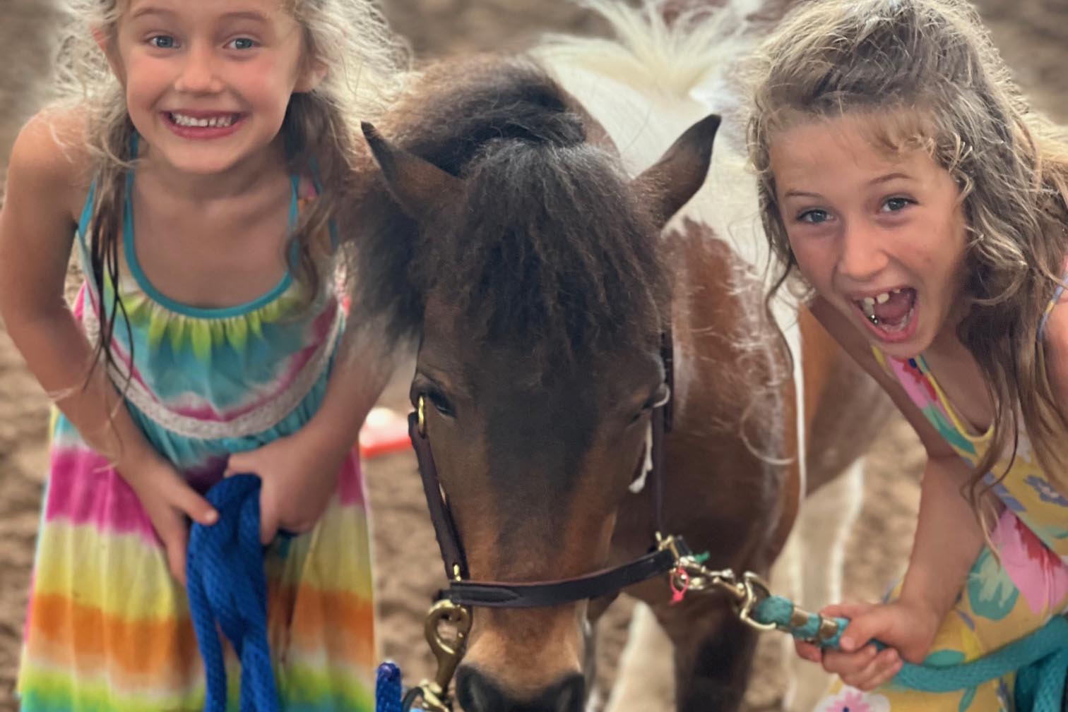 MagicalMoment Two happy smiling girs in summer dresses with The Peace Ponies Sheriff a mini horse at a Magical Moments With The Peace Ponies experience at Pine Knoll Farm